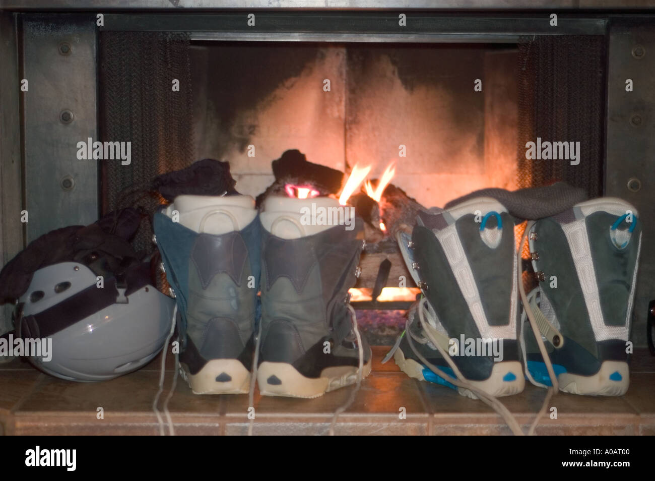 A color horizontal image of snowboard boots and a helmet drying in front of a fire Stock Photo