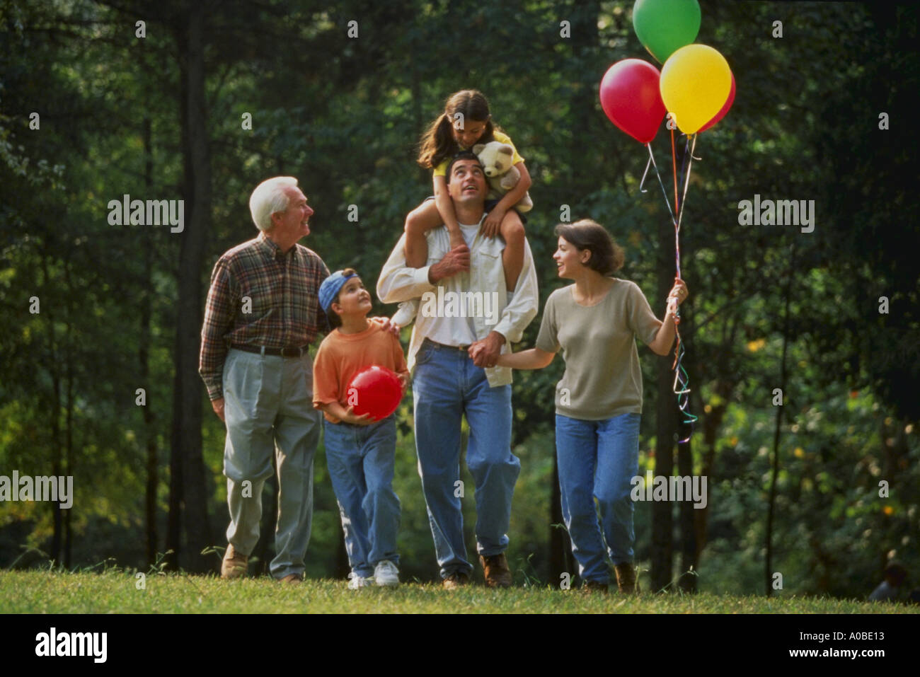 Three generations of a family with grandfather parents and three children walking in the park with balloons Stock Photo