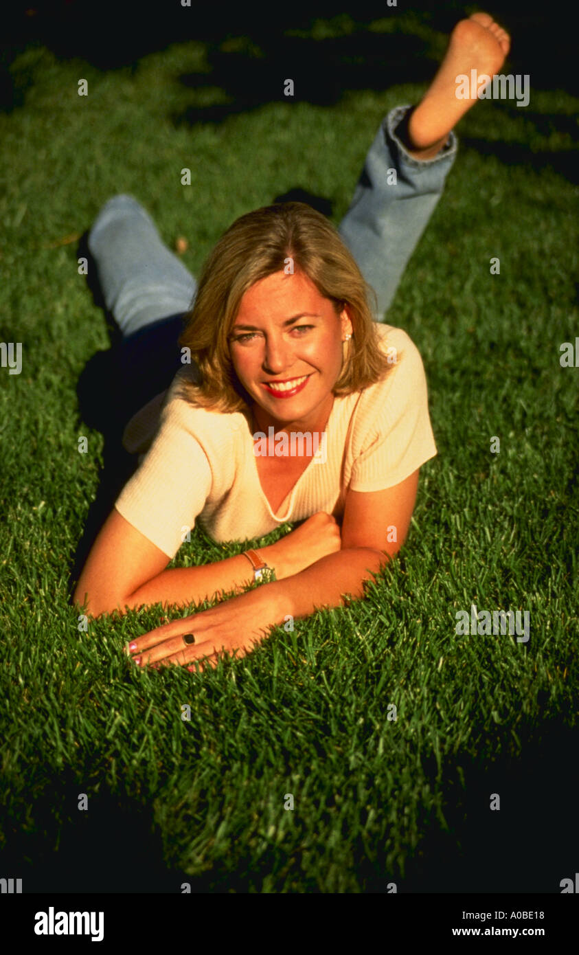 Portrait of a smiling woman laying in the grass with her foot up behing her Stock Photo