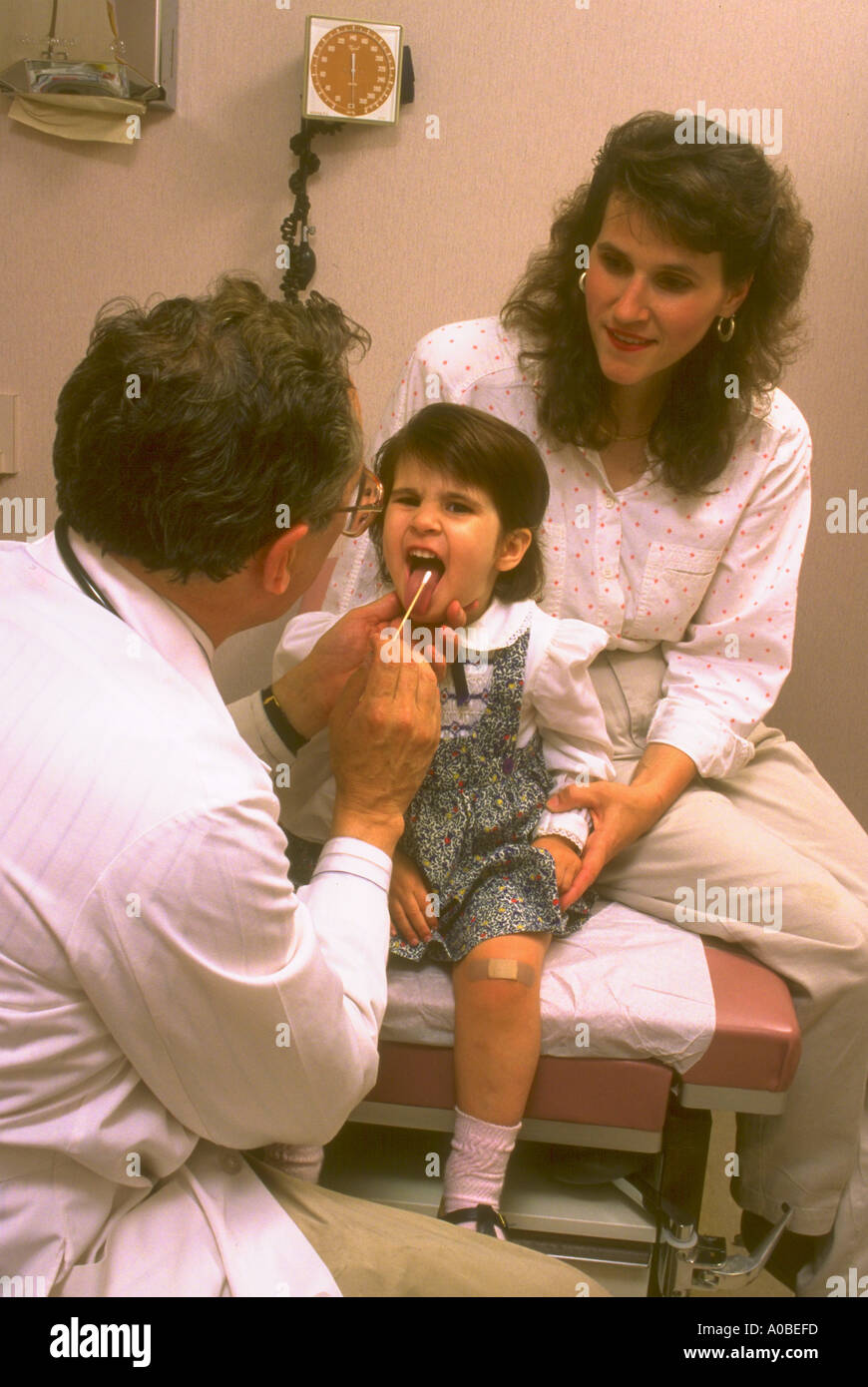 Pediatrician examines child in office while mother looks on Stock Photo