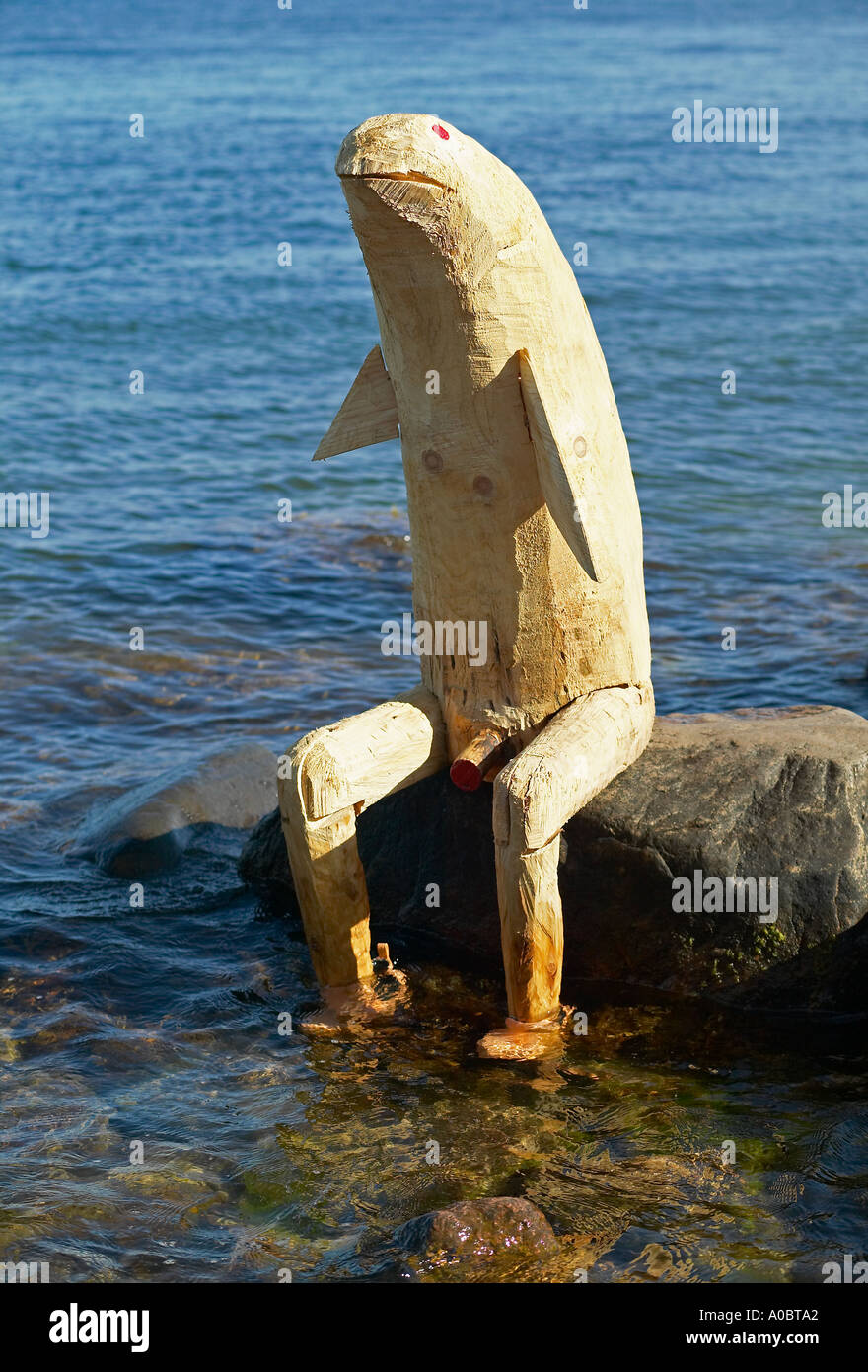 Funny wooden sculpture sitting on rock beside the little Mermaid statue, Copenhagen, Denmark, Europe Stock Photo