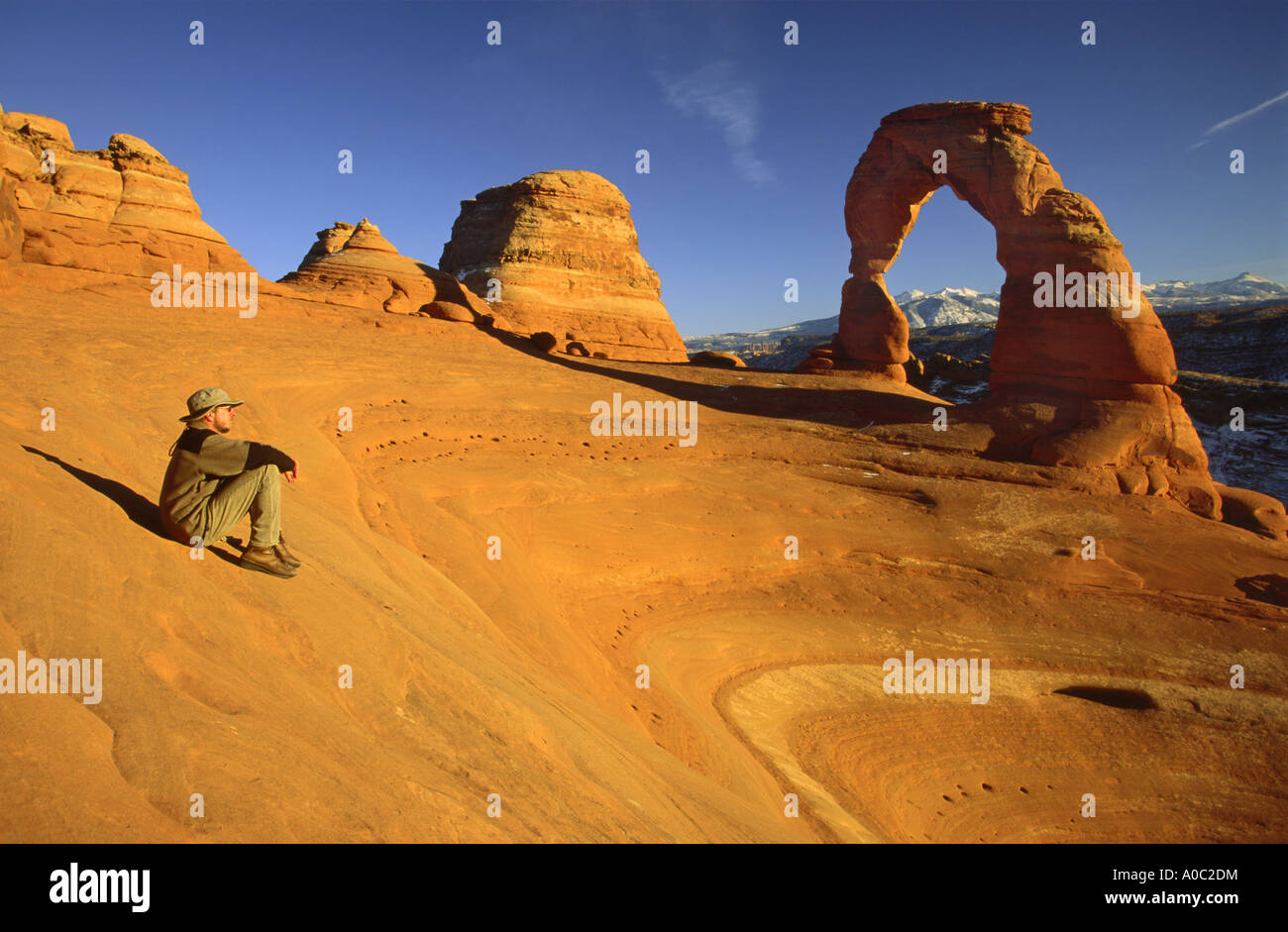 Hiker near Delicate Arch in winter, La Sal Mts in dist, Arches Nat Park, Utah, USA Stock Photo