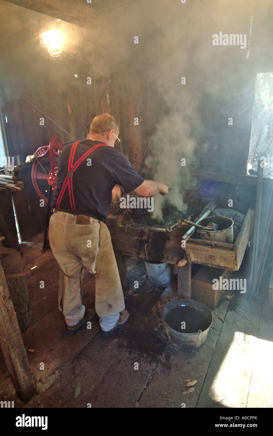 The shack fills full of smoke as a blacksmith prepares the coal fed fire before working on a metal tool at a saw mill in Occiden Stock Photo