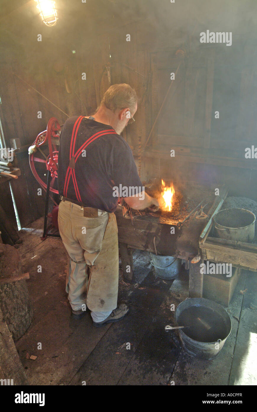 A blacksmith begins heating a piece of metal in the coal fed fire to make a custom tool at a saw mill in Occidental California Stock Photo