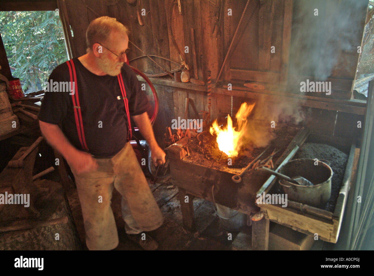 A blacksmith pumps more air into the coal fed fire to make it burn hotter as he heats metal to make a custom tool at a saw mill Stock Photo