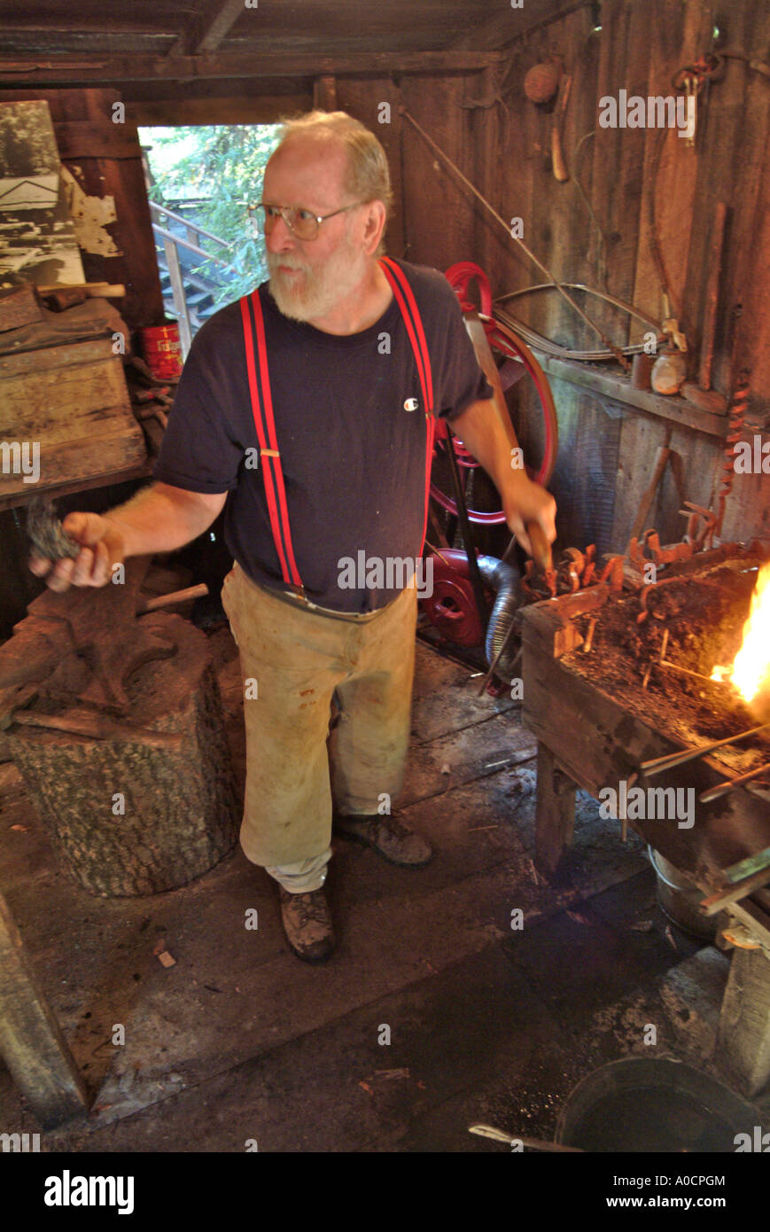 A blacksmith pumps more air into the coal fed fire to make it burn hotter as he heats metal to make a custom tool at a saw mill Stock Photo