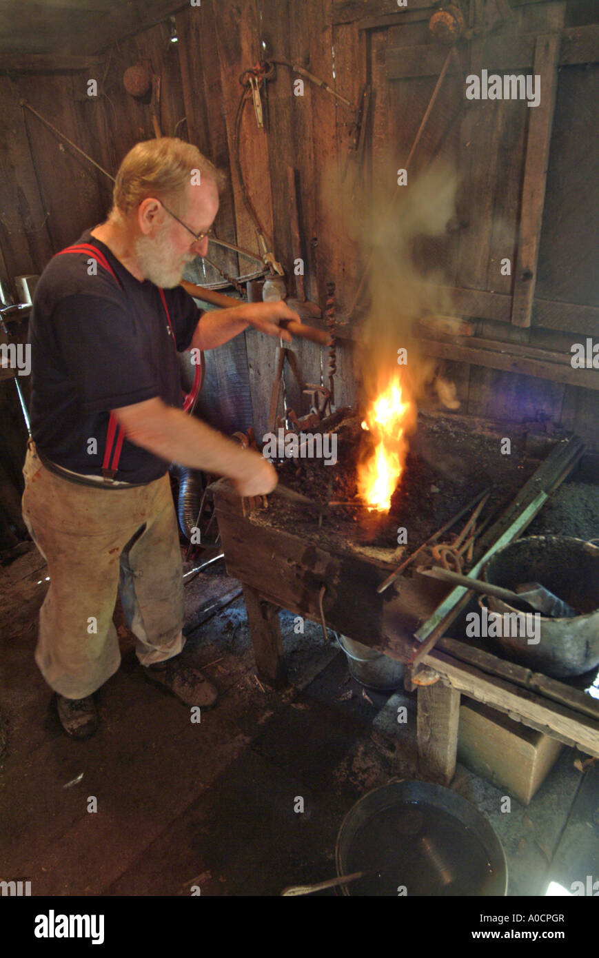 A blacksmith pumps more air into the coal fed fire to make it burn hotter as he heats metal to make a custom tool at a saw mill Stock Photo