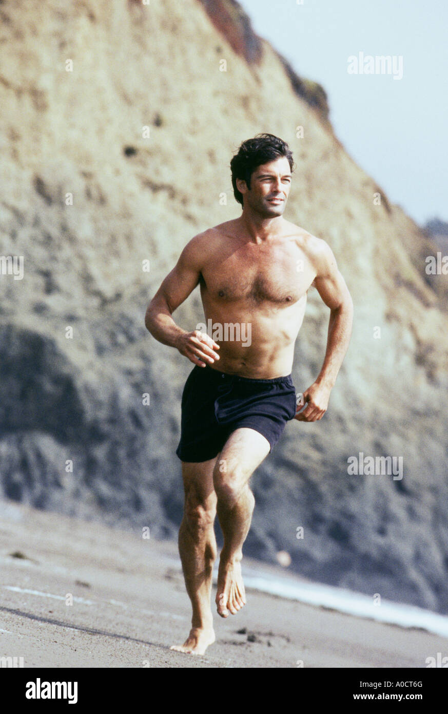 Shirtless man running on beach with rocky cliffs Stock Photo Alamy