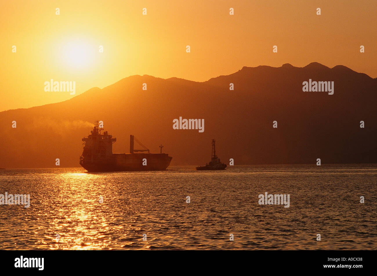 A ship being towed by a tug out of port at sunset Subic Bay Freeport Zone Luzon Philippines Stock Photo