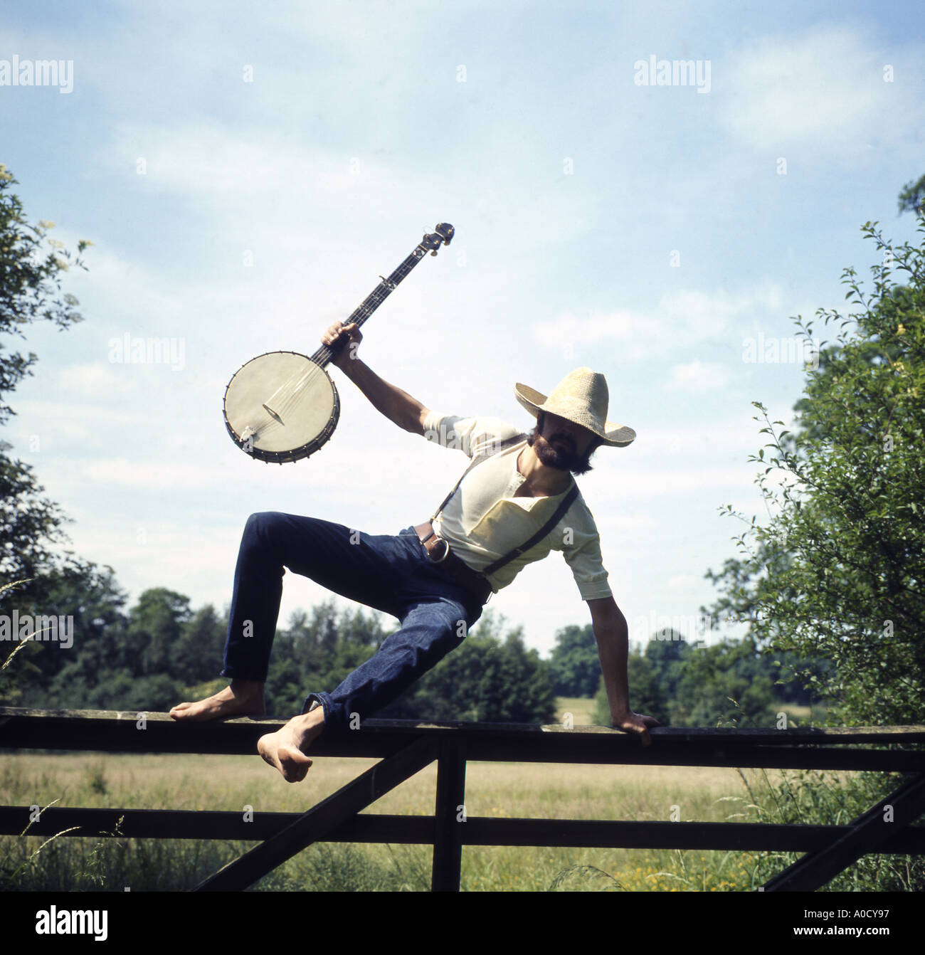 Man Leaping Over a Gate Holding a Banjo Aloft Stock Photo