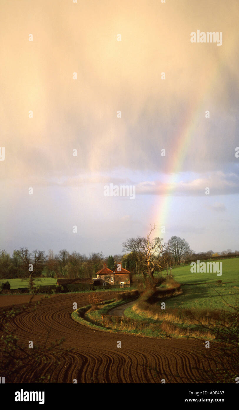 rain shower with rainbow passing over farmhouse and fields coltishall norfolk uk Stock Photo