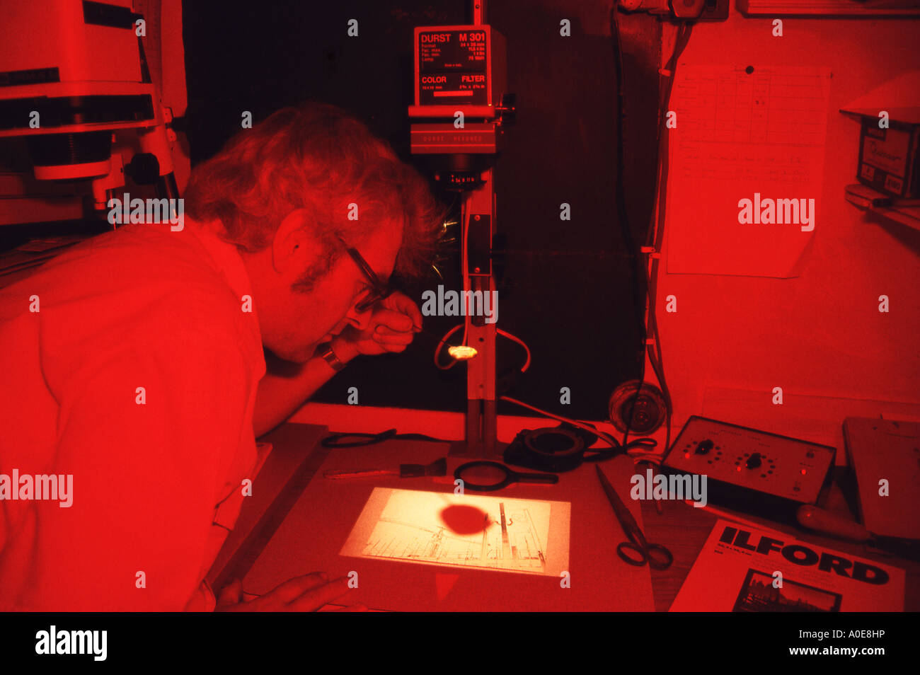 Man in red safelight of darkroom focusing and composing an image on