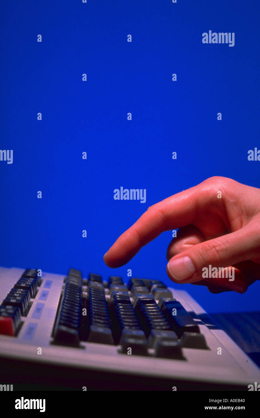 Hand with index finger pointing a computer keyboard about to hit a key Stock Photo