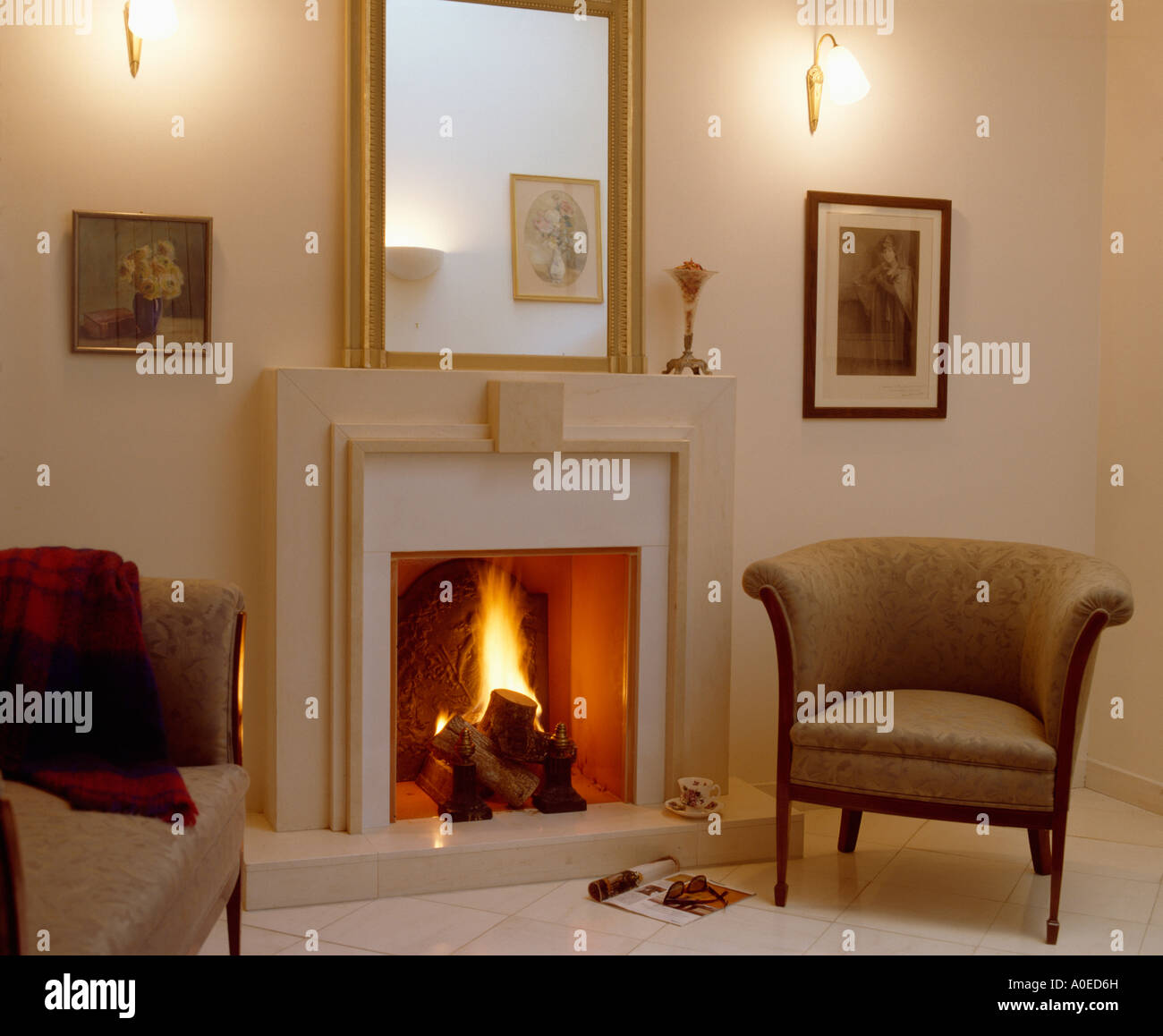 Wall-lights above modern fireplace with lit fire and armchair on right ...
