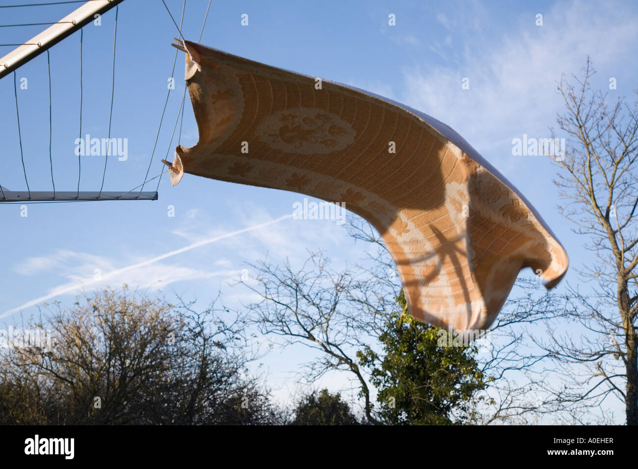 Large towel hanging out to dry with pegs on rotary washing line blown horizontal by strong wind with sun and blue sky Stock Photo