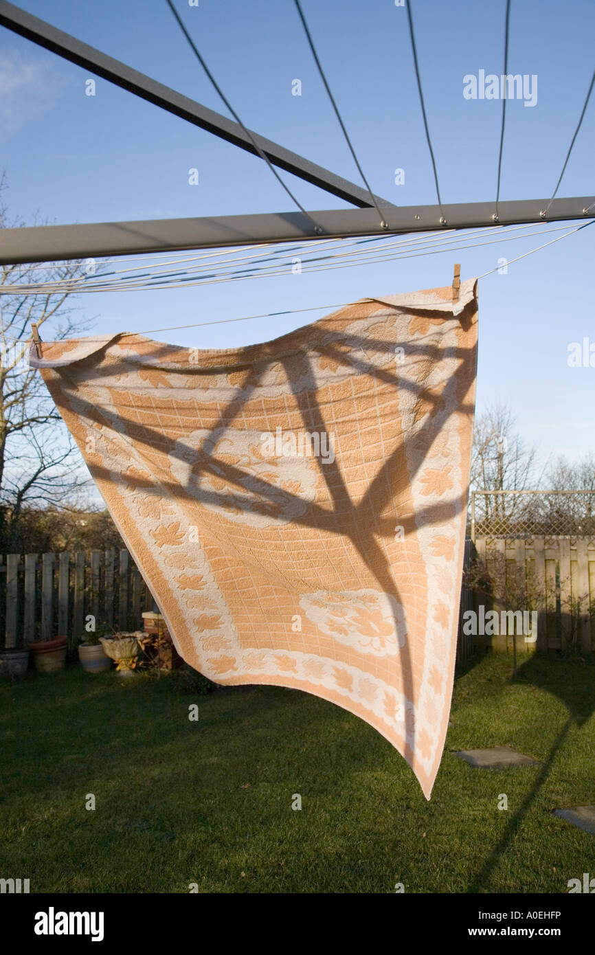 Large towel hanging out to dry with pegs on rotary washing line blown by wind with sun and blue sky Stock Photo