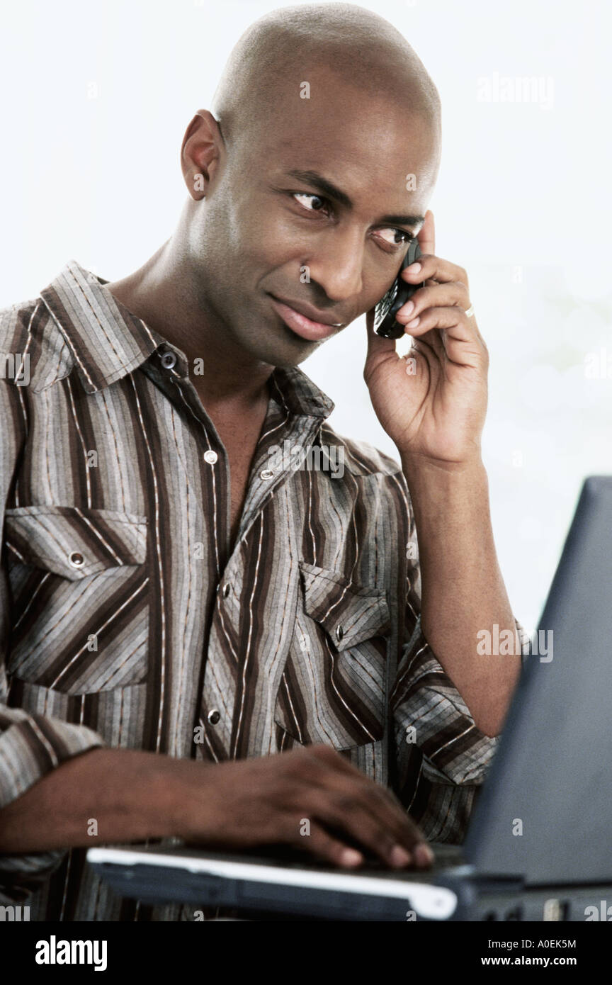 Man working on laptop computer while using mobile phone Stock Photo
