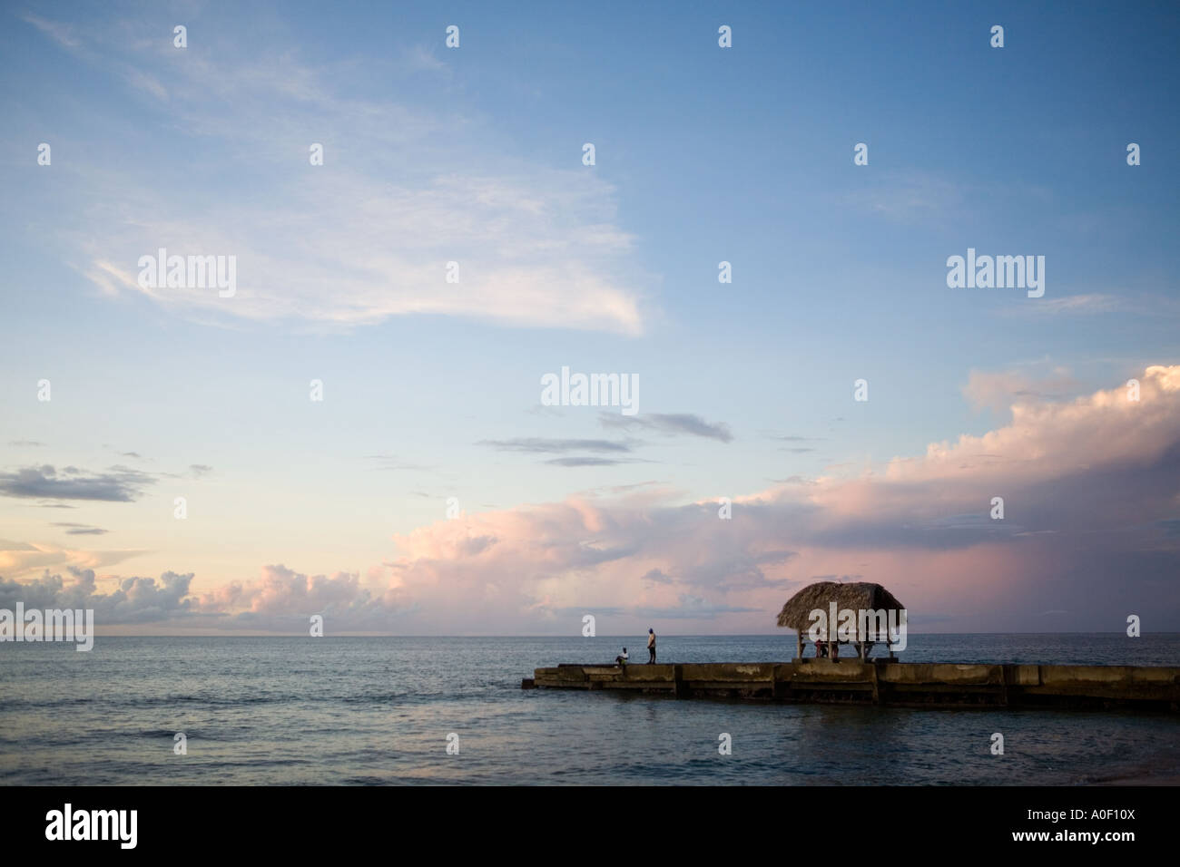 Sun setting over the ocean behind jetty and palm covered shelter , Tobago Island, Caribbean Stock Photo