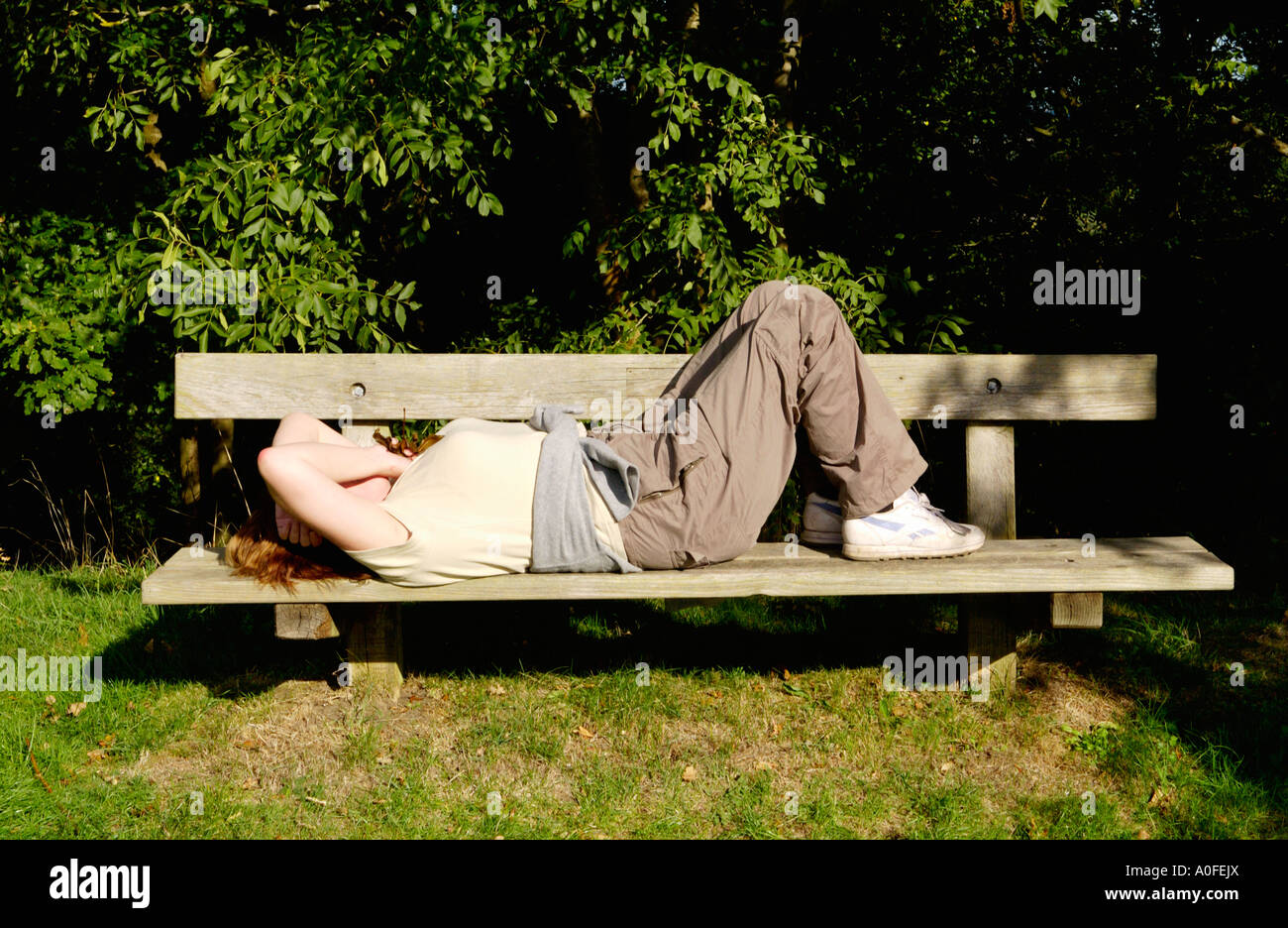 Young woman relaxing in sun lying on bench in countryside near Knightwick Worcestershire England Stock Photo