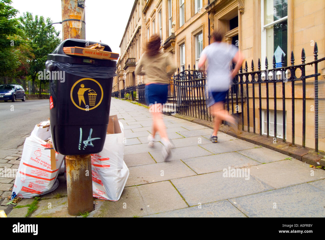 Joggers running past rubbish left on sidewalk Stock Photo