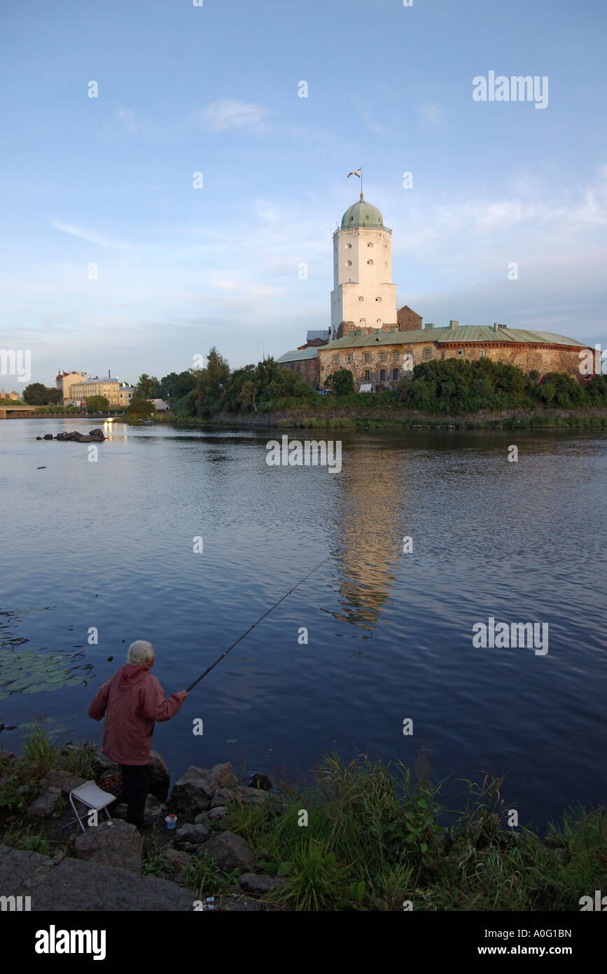 Old lady fishing in Vyborg St Olaf s tower in background Russia Stock Photo