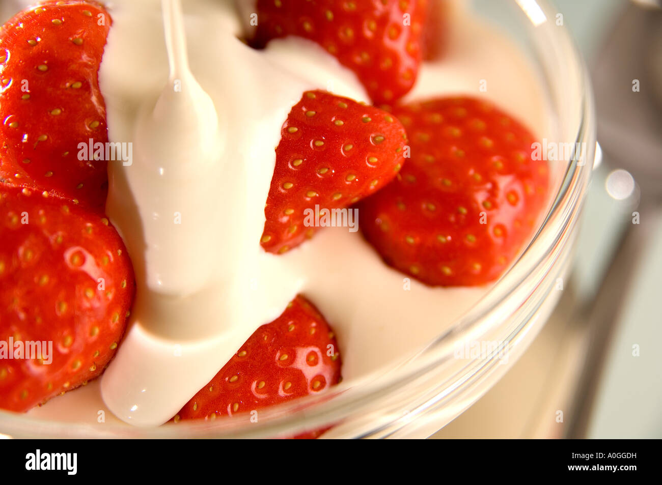 Dribble of cream over strawberries in a glass bowl with out of focus spoon below Stock Photo