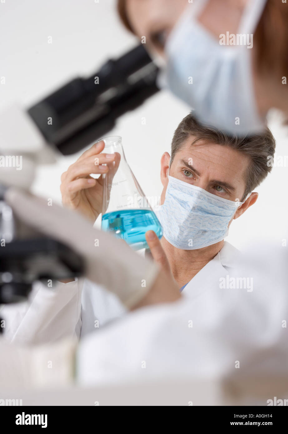 Scientists with microscope and blue liquid Stock Photo