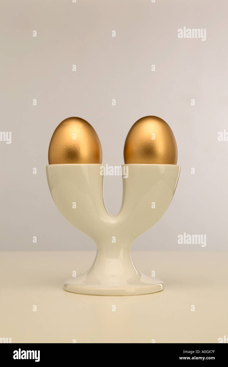 TWO GOLD EGGS IN DOUBLE WHITE EGG CUP Stock Photo