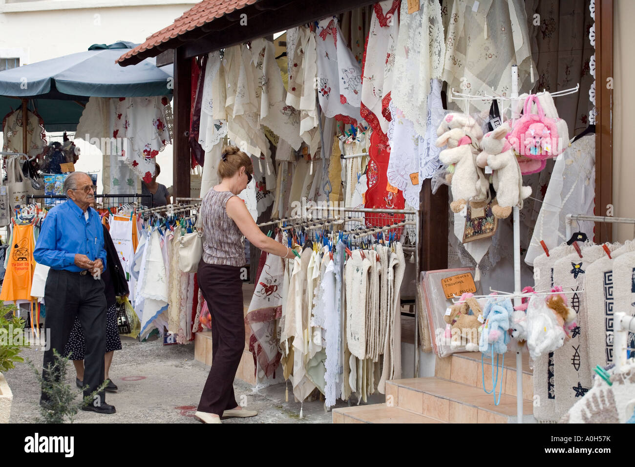 A WOMAN TOURIST LOOKS AT LOCAL LINEN AT THE MARKET IN PAPHOS, CYPRUS Stock Photo