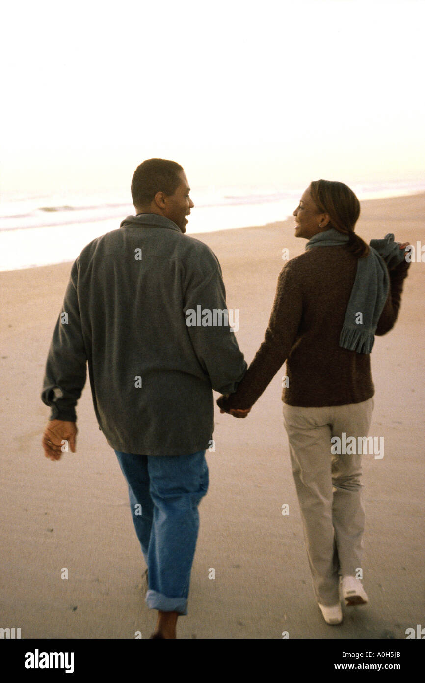 Rear view of a young couple walking on the beach holding hands Stock ...