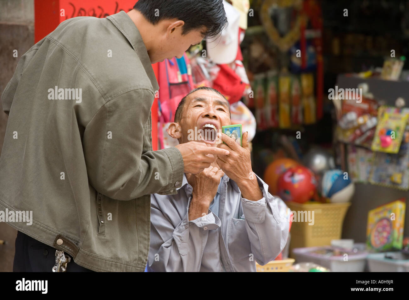 Chinese minority man checks the work of a street dentist, Xinjie market, Yuanyang, Yunnan, China Stock Photo