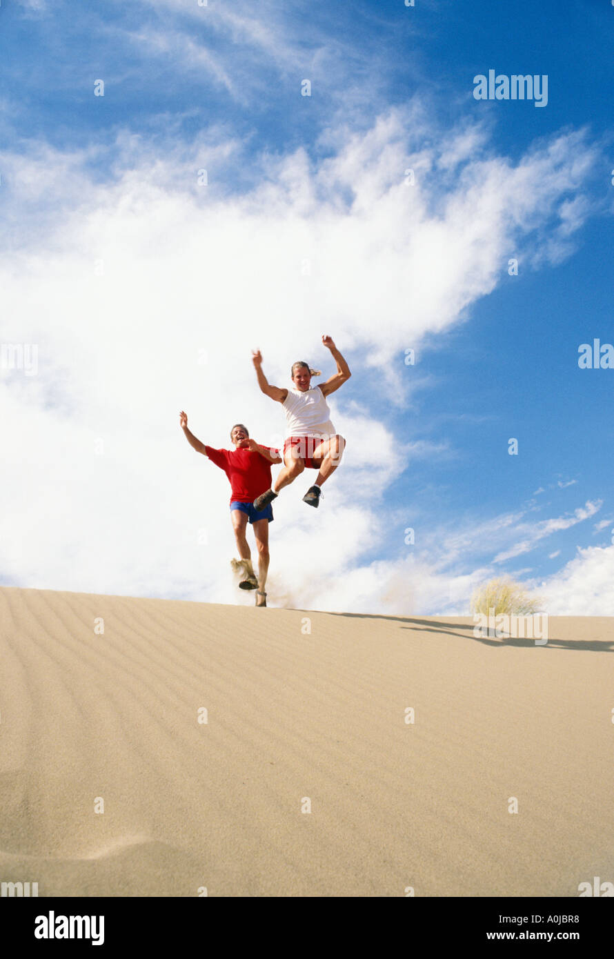 Two men leaping from sand dunes Stock Photo