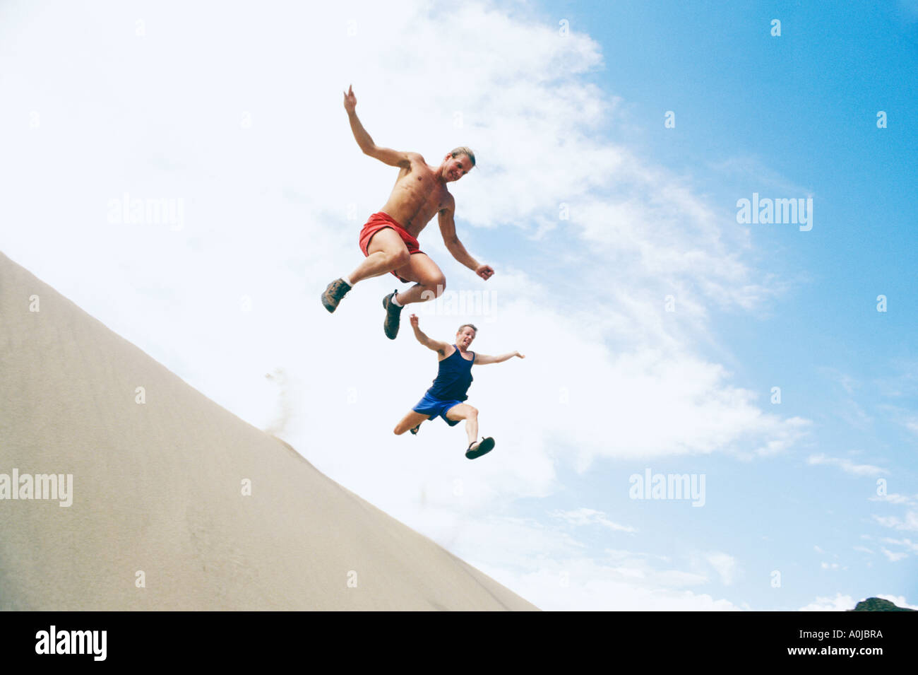 Two men leaping from sand dunes Stock Photo