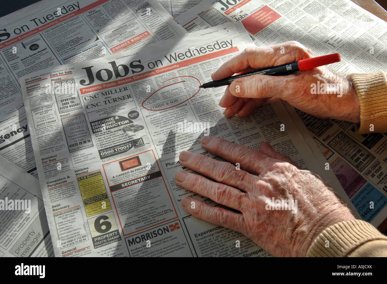 Hands of an elderly man holding a pen he is using to circle jobs in classified adverts Stock Photo