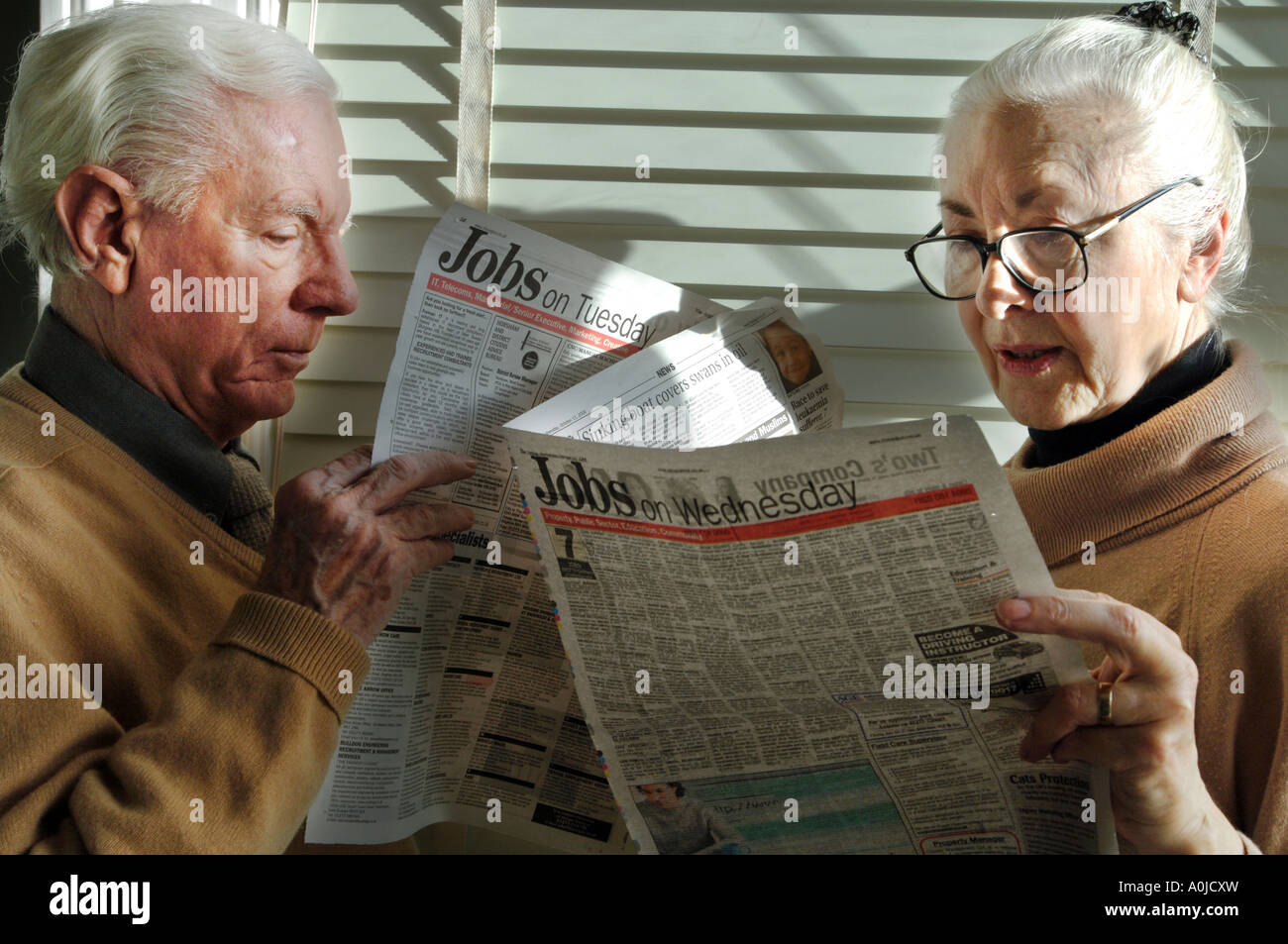 Two pensioners, a man and a woman, look at job ads in a paper, trying to find jobs to suppliment tiny pension payments. Stock Photo