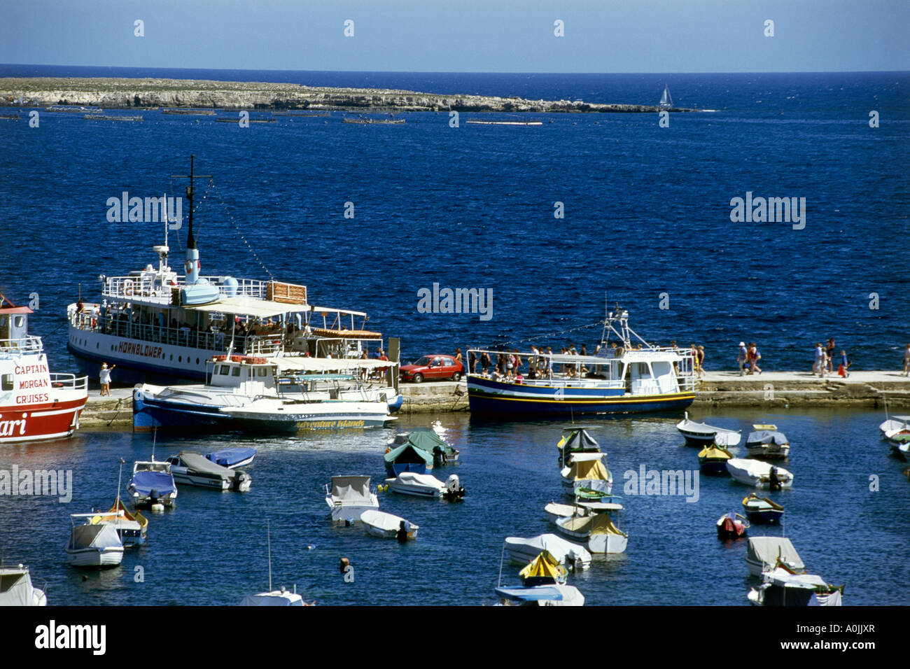 Pedalos and pleasure boats at their moorings in the crystal clear waters surrounding the rocky seafront at the small town of Bugibba on Malta s north coast Stock Photo