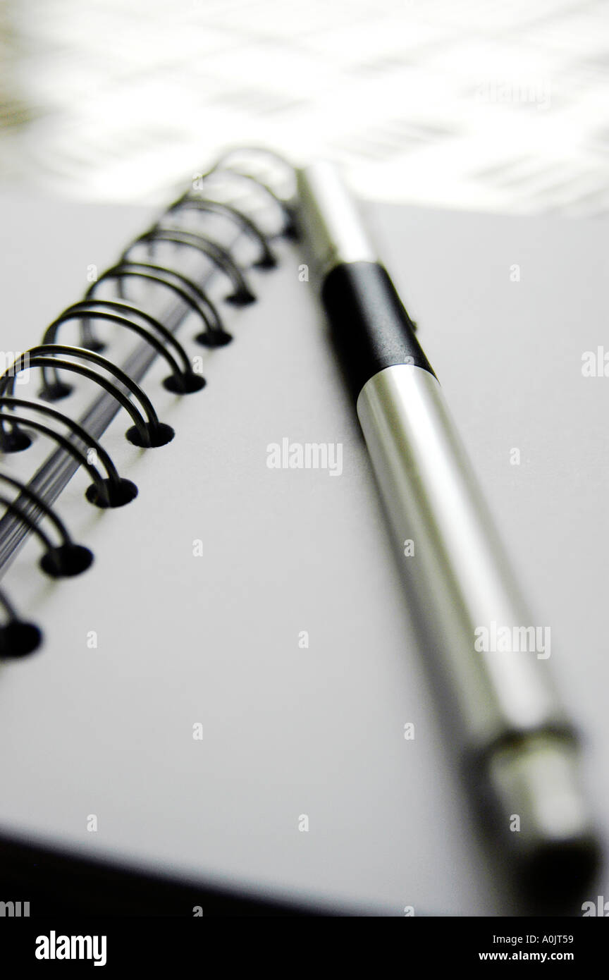 White note book with black spiral binding, stainless steel pen. Shot on funky punched stainless steel table top. Stock Photo