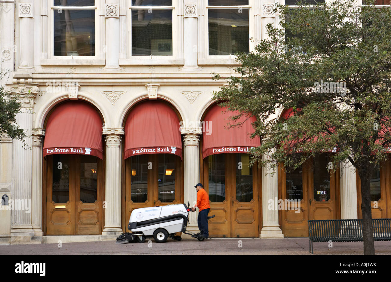 TEXAS Austin Man stand on back of motorized sidewalk cleaner brushes clean outside IronStone Bank building Congress Street Stock Photo