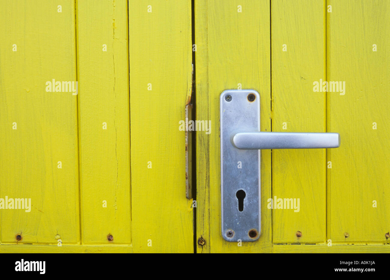 Close up detail of bright yellow stained wooden door on a hut or shed or kiosk or booth with aluminium door handle Stock Photo