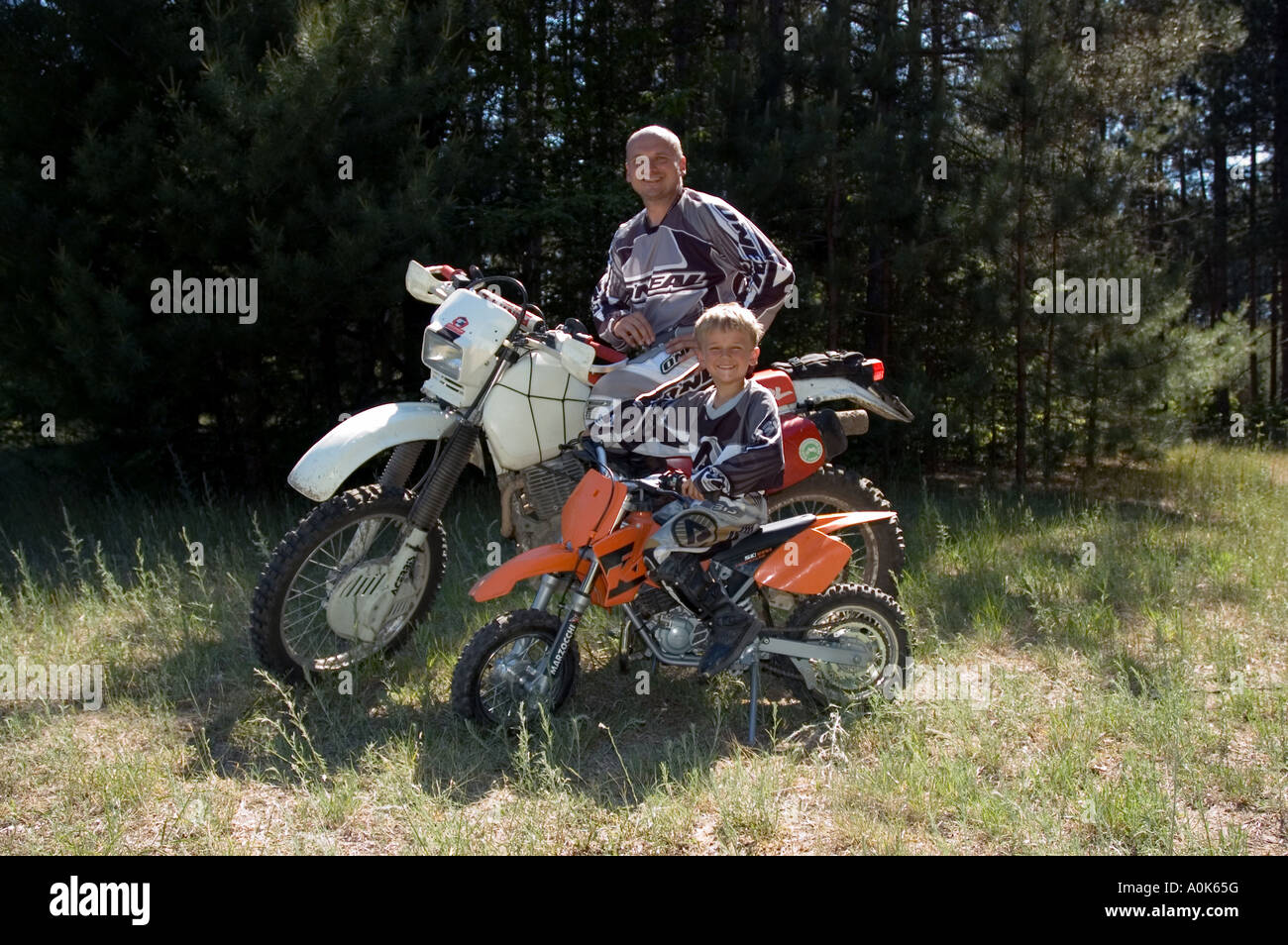 Caucasian Father and 6 year-old Son pose for photo on their dirtbikes 2, in forest, Northern Michigan, USA Stock Photo