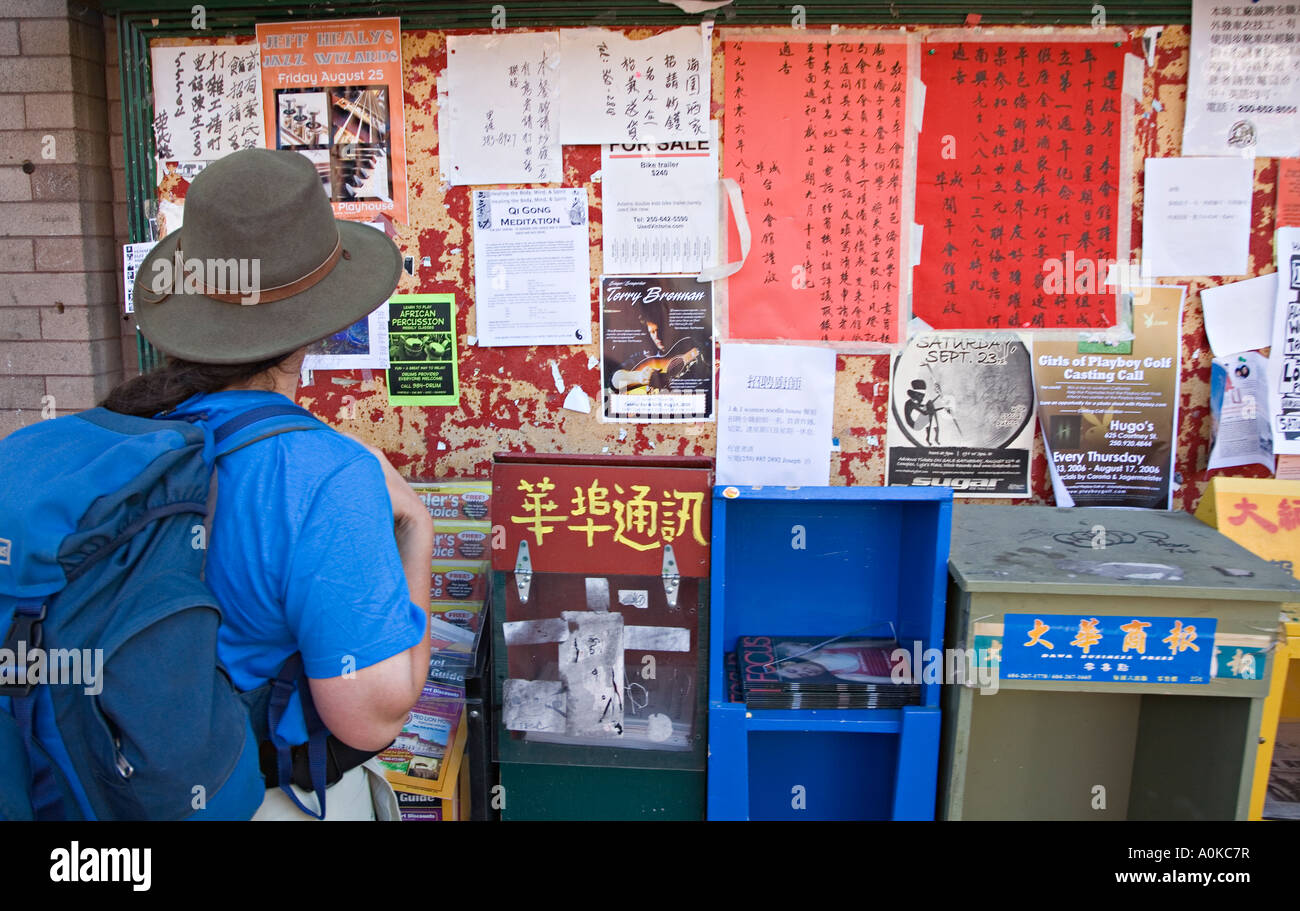 Backpacker looking at Chinese posters and signs stuck to wall in Chinatown Victoria Canada Stock Photo
