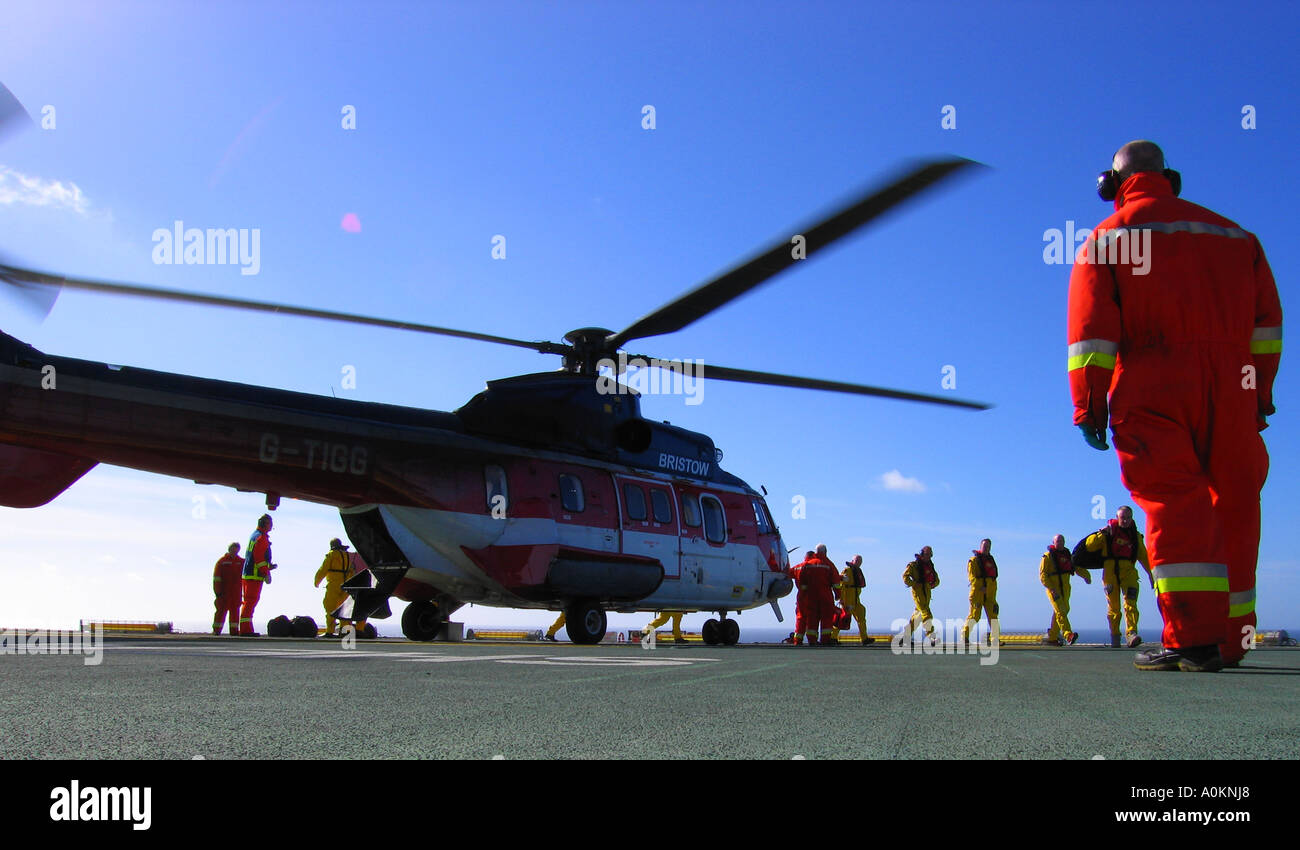 A North sea helicopter on deck with passengers disembarking and deck crew unloading baggage. Stock Photo