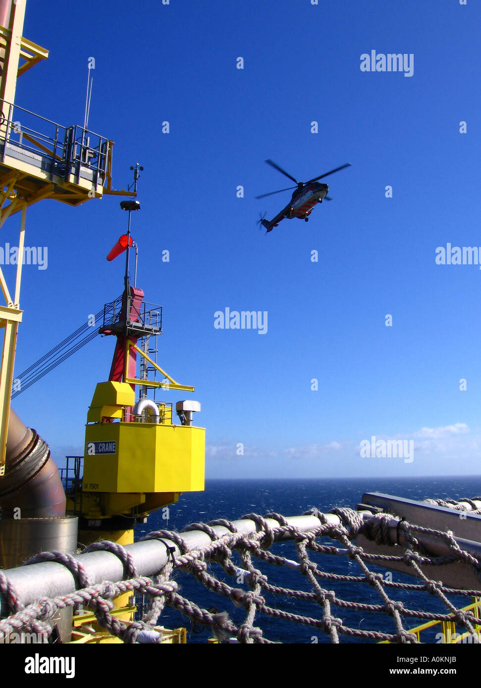 A helicopter coming in for landing on a North sea oil rig against a deep blue sky in portrait format. Stock Photo