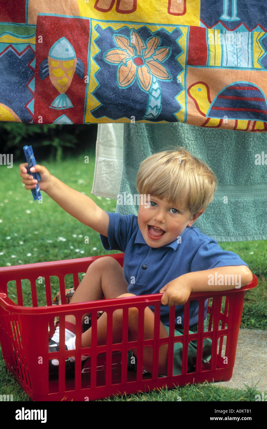 young child helping to hang out the washing sat in the basket passing pegs Stock Photo