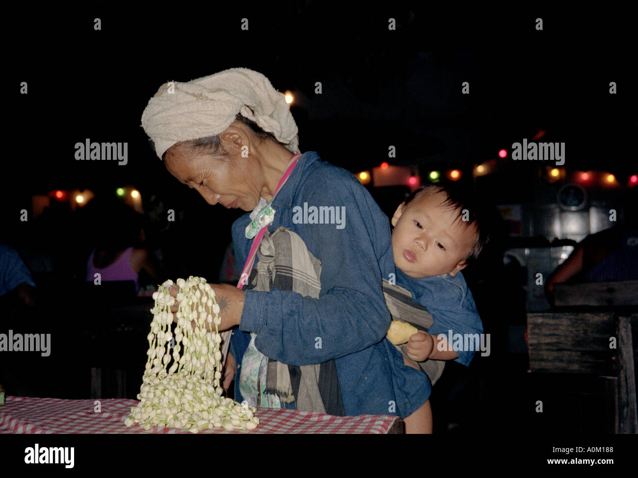 Woman selling flower necklaces in Chang Mai Thailand while carrying a child on her back Stock Photo