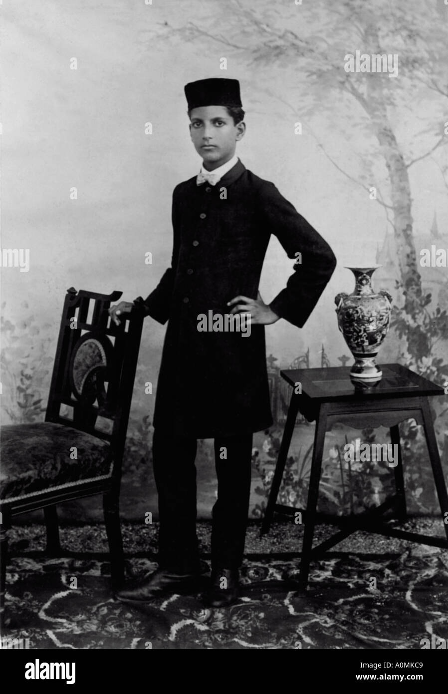 Old Historical Picture of one man dressed in old suit with pant standing with a chair India Stock Photo