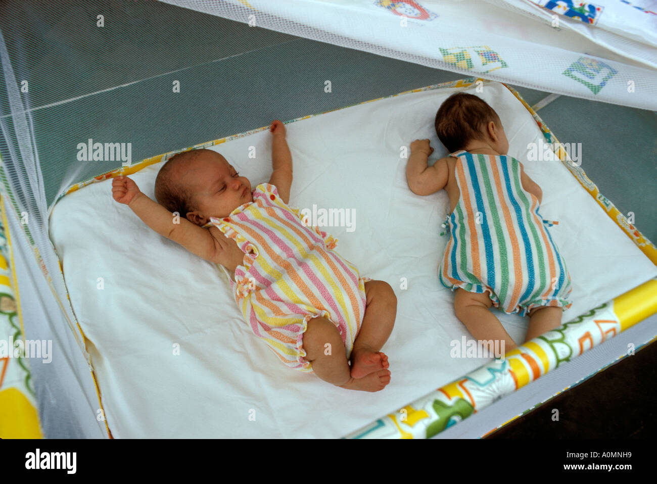 2 two twin girls nap in net covered playpen on roof Stock Photo