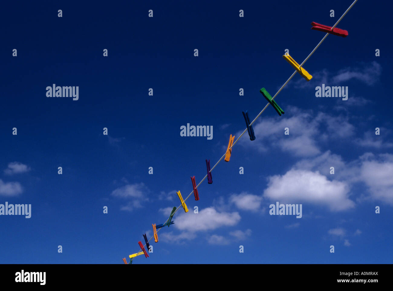 Multi colored clothespins hanging on a clothesline with white clouds and blue sky Stock Photo