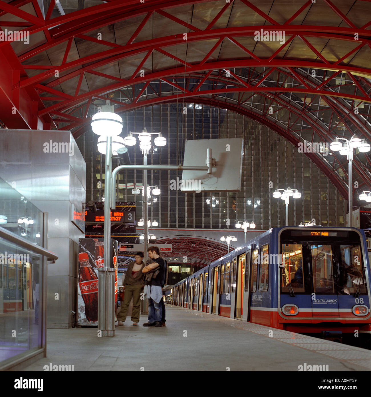Night shot of DLR platform at Canary Wharf Station, Tower Hamlets London inc. elliptical glass metal roof DLR train passengers Stock Photo