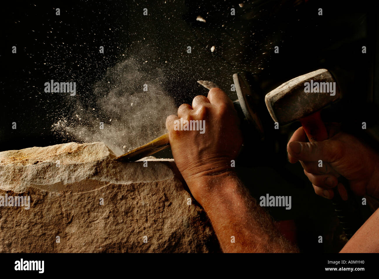 A stonemason works with hammer and cold chisel in studio light Stock Photo